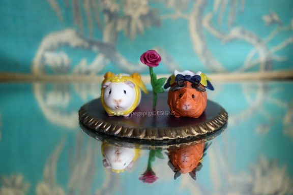 Zwei Meerschweinchen als Belle und das Biest auf einer Basis mit einer Miniatur Rose im Hintergrund