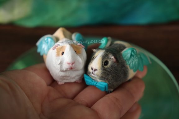 Rosetten Meerschweinchen Figur in weiß und creme zusammen mit Mehrfarbigem Agouti Meerschweinchen mit blauer Fliege und Flügeln