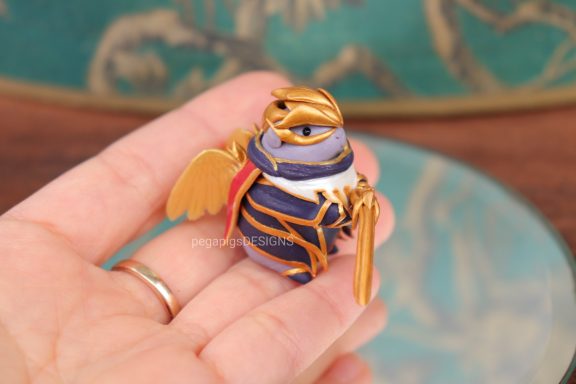 Meerschweinchen Figur mit Rüstung in lila und gold mit einem Gewehr.