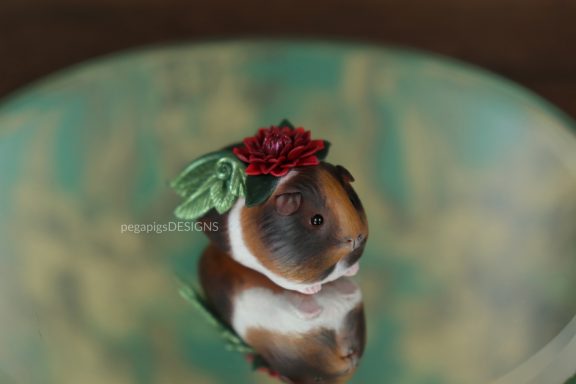 Mehrfarbige Meerschweinchen Skulptur mit grünen Flügeln und einer roten Blume