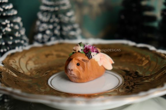 Hellbraune Meerschweinchen Figur mit Flügeln und Blumen auf einem Teller