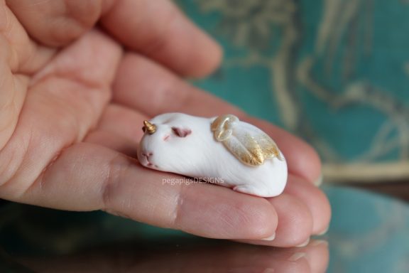 Schlafendes weißes Meerschweinchen als Miniatur Skulptur mit gold-weißen Flügeln und einem goldenen Horn