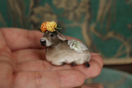 Graue Kuh Skulptur mit Flügeln und gelber/orangener Pfingstrose auf dem Kopf